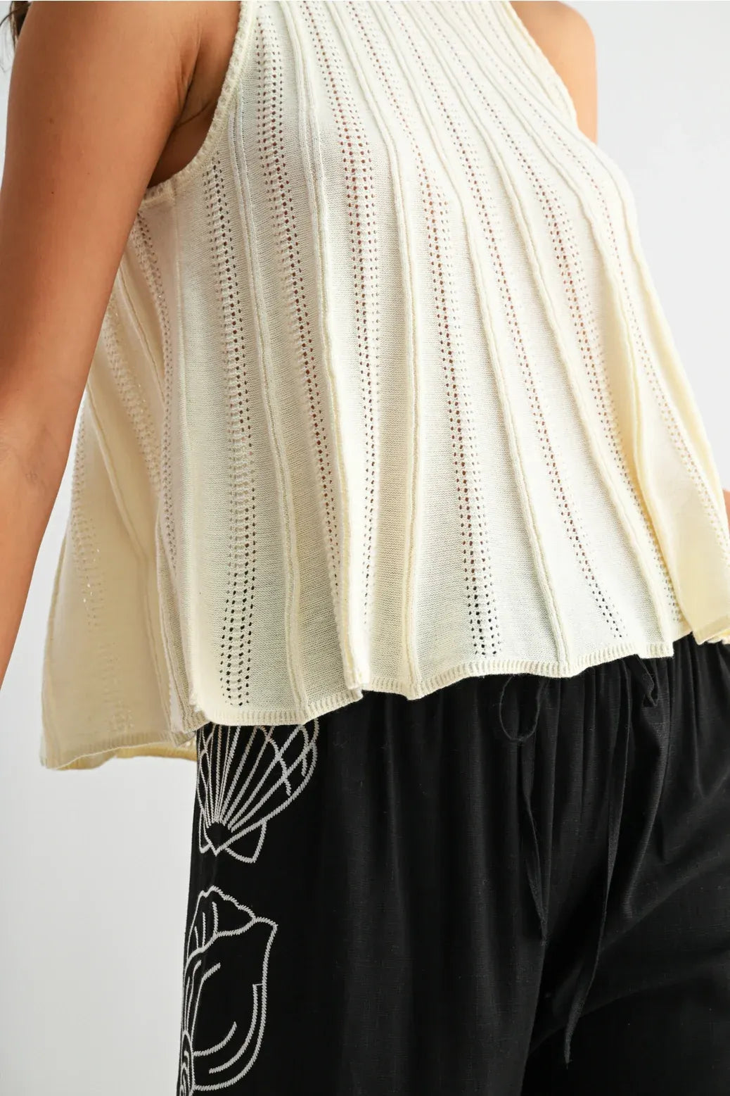 Cream-colored ribbed knit flared hem sleeveless top with peplum hem and delicate eyelet detailing