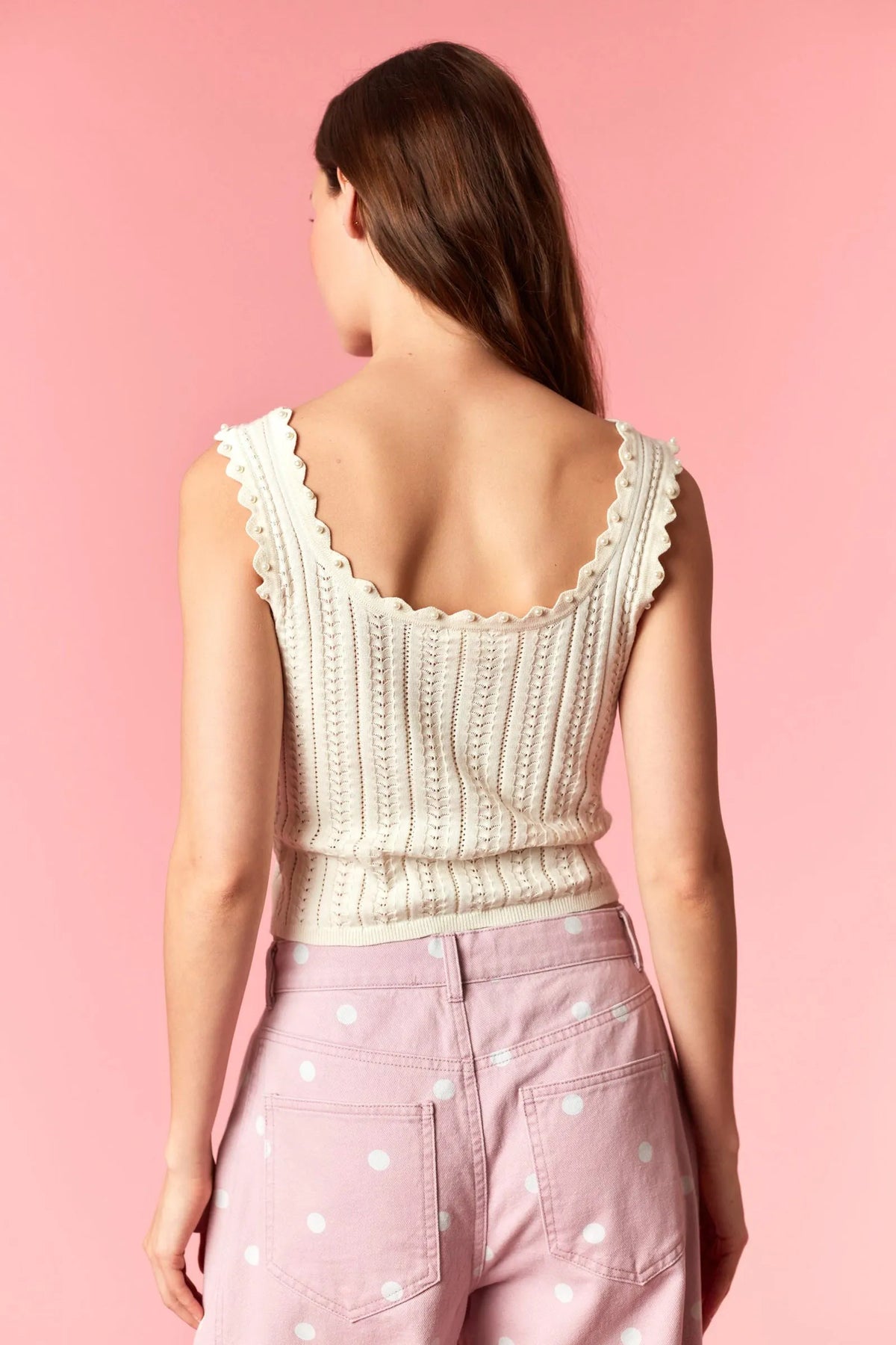 A cream-colored ribbed knit tank top with scalloped neckline featuring pearl studs for elegant style