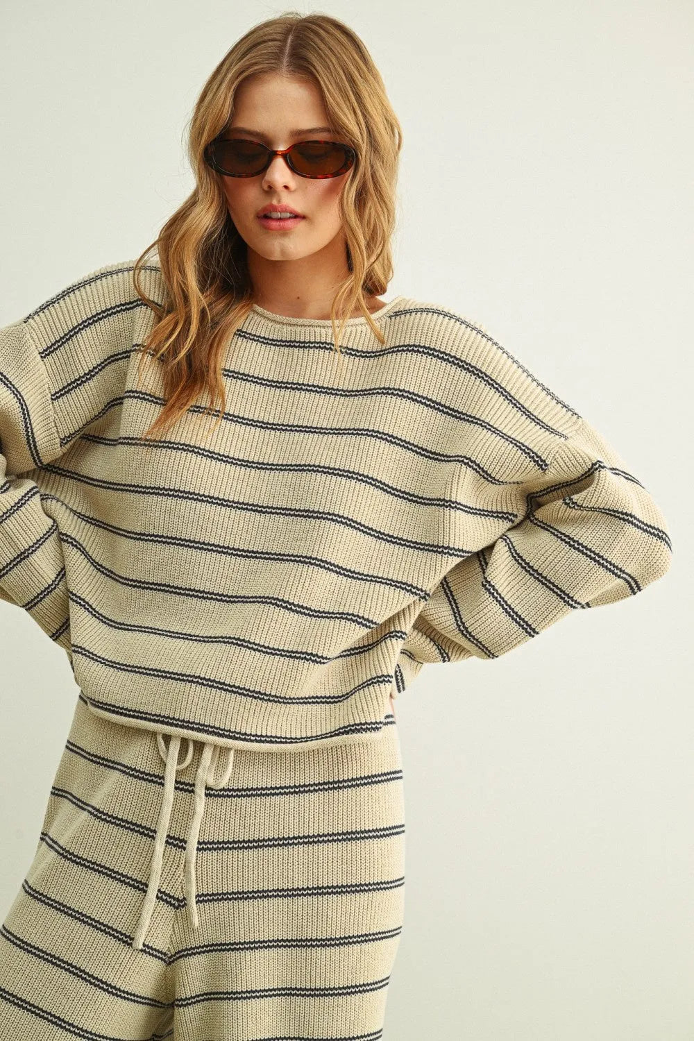 Cream-colored ribbed knit striped pattern long sleeve sweater with black horizontal stripes and drawstring waistband