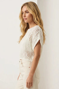 A cream-colored, short-sleeved knitted crop top with openwork pattern and relaxed fit in ballast crochet sweater style