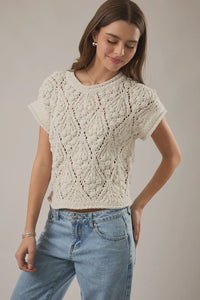 Cream-colored short-sleeved knitted extended shoulder sweater top with intricate diamond-patterned lacework