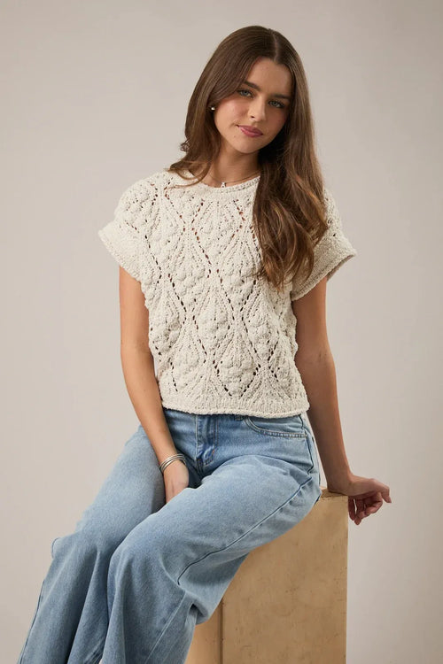 Cream-colored extended shoulder sweater top in knitted fabric featuring intricate diamond-patterned lacework