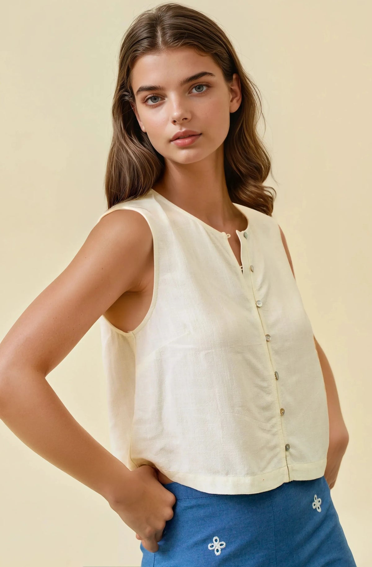 Cream-colored sleeveless viscose blend button front top with subtle sheen and delicate floral embroidery on hem