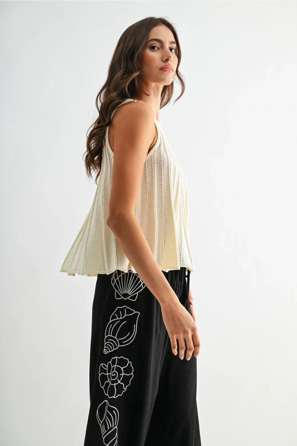 Cream-colored flared hem sleeveless knit top with delicate vertical perforations and peplum hem design