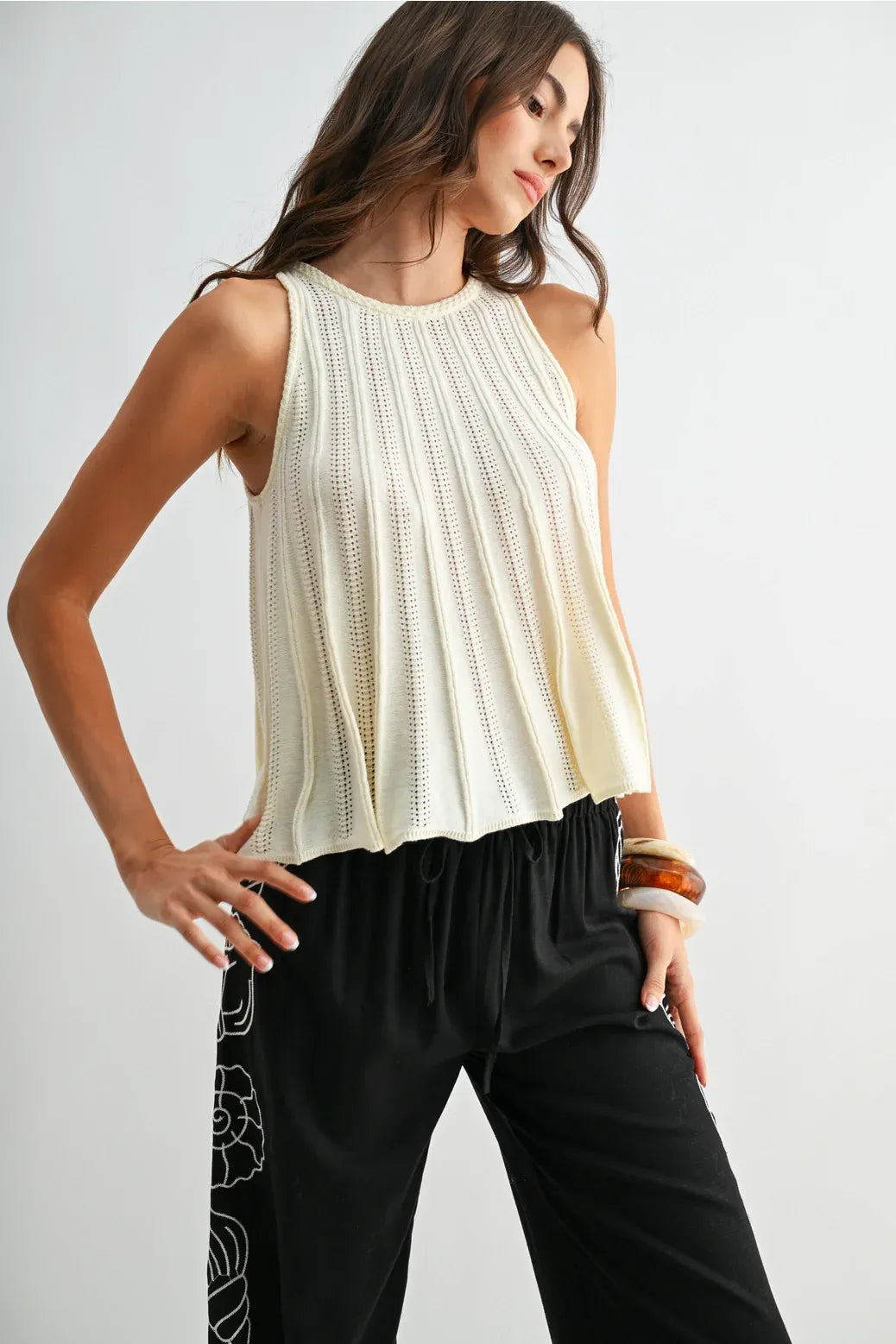 Cream-colored flared hem sleeveless knit top with vertical pleats and relaxed fit in soft knit fabric