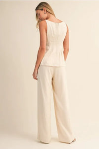 Cream-colored sleeveless peplum scoop neck blouse with zipper back and subtle pleating in structured design