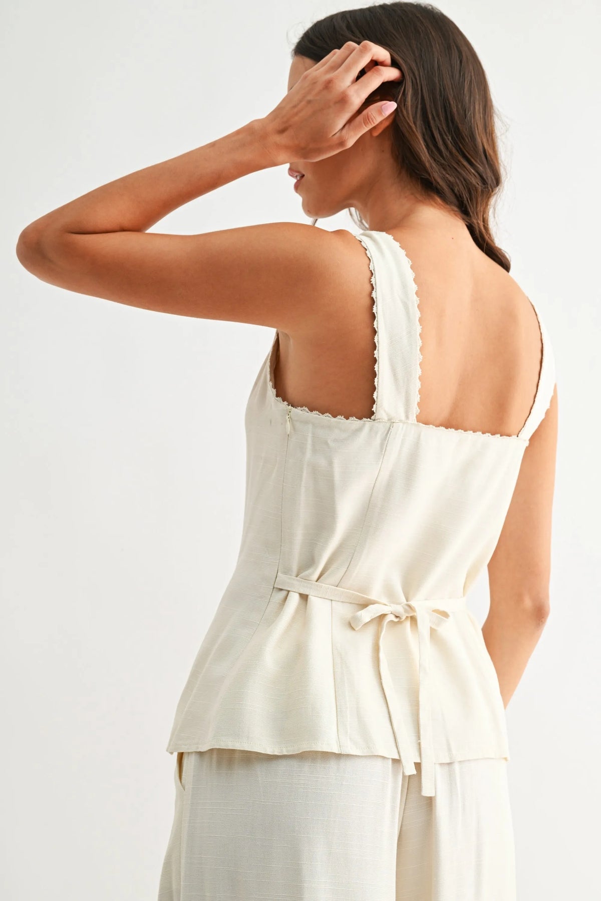 Cream-colored sweetheart button-down vest with scalloped shoulder straps and a tied waistband sleeveless top