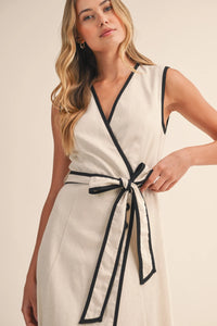 Cream-colored sleeveless midi dress with contrast piping wrap design and matching belt tied at the waist
