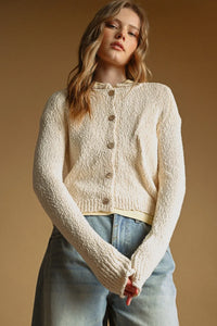 Cream-colored textured knit cardigan with button closure featuring a classic sweater knit cardigan design