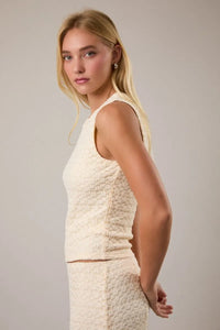 Cream-colored fitted cropped sleeveless top with round neck lace detailing and textured fabric for elegant wear