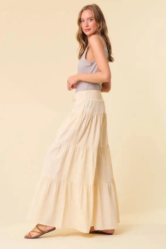 Cream-colored tiered wide pants with smocked waist and soft flowing fabric featuring gentle ruffles at each layer