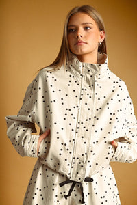 A cream-colored polka dot high neck jacket with a drawstring waist and high collar trench coat design