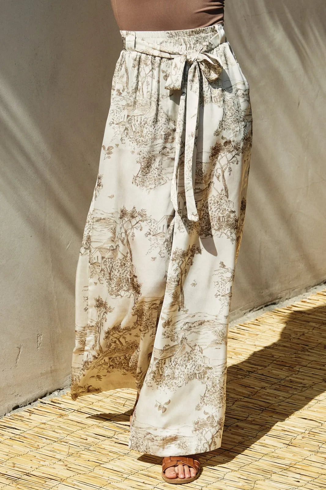 Cream-colored printed belted wide leg pants with brown and beige toile print and elastic waistband with fabric belt