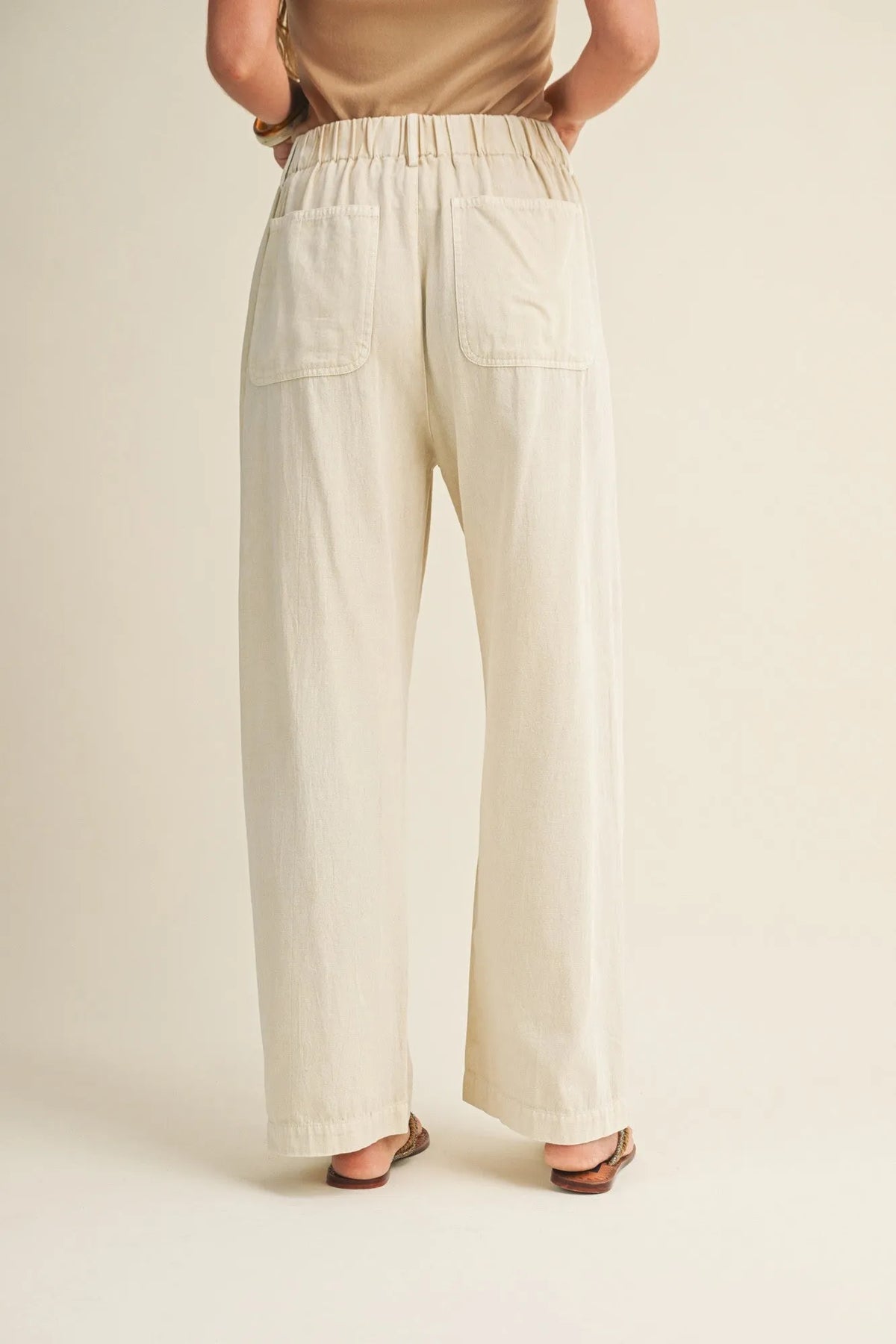 Cream-colored pleated waist wide leg dyed pants shown from the back with elastic waistband and two back pockets