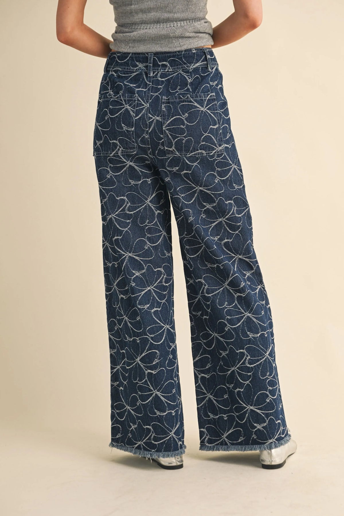 Dark blue denim wide-leg pants with white floral design and distressed hem featuring frayed edges