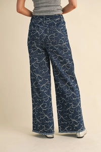 Dark blue denim wide-leg pants with white floral design and distressed hem featuring frayed edges