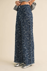 Dark blue denim wide-leg pants with white floral design distressed hem featuring embroidered four-leaf clovers