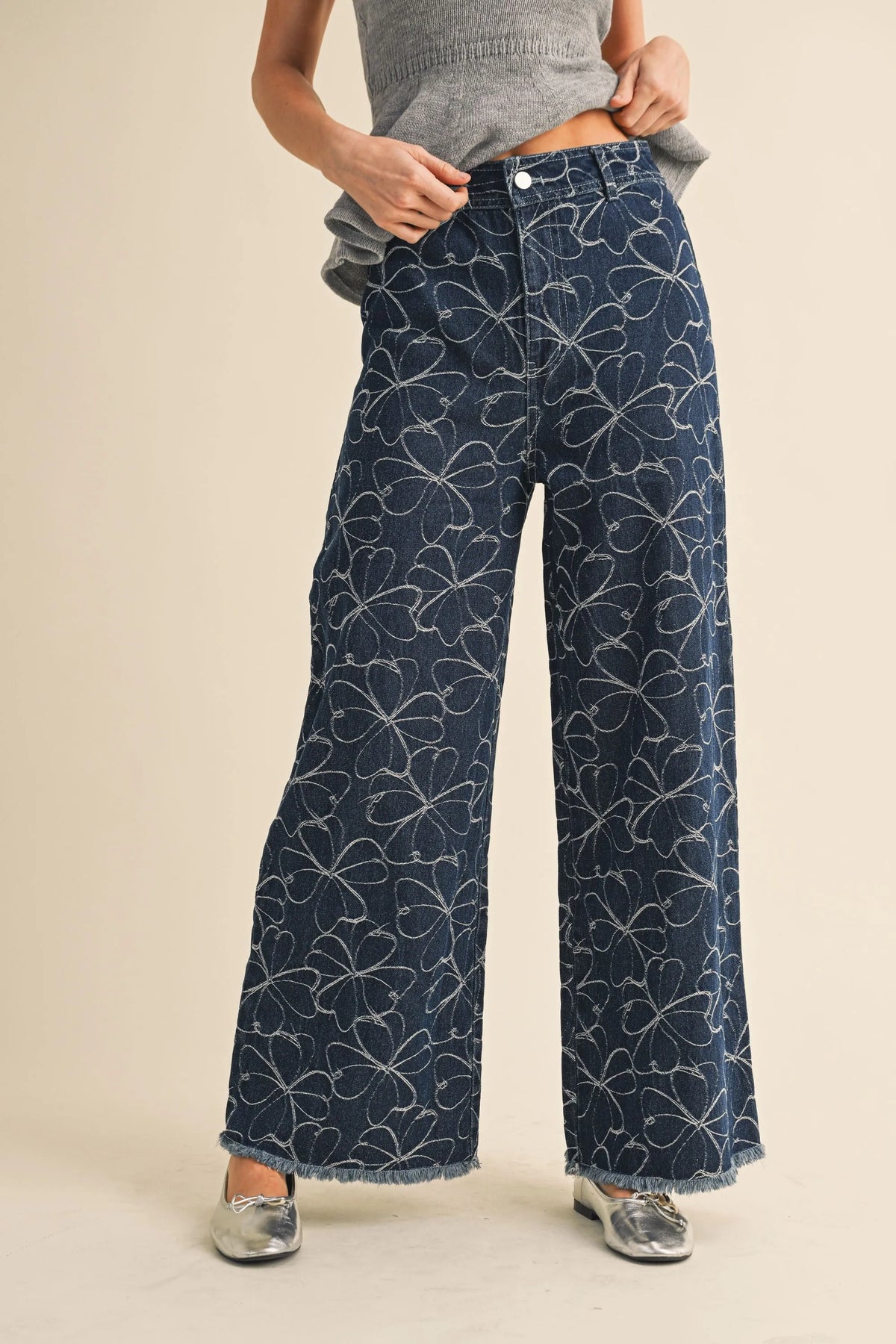 Dark blue denim wide-leg pants with subtle white floral design and distressed hem for a stylish look