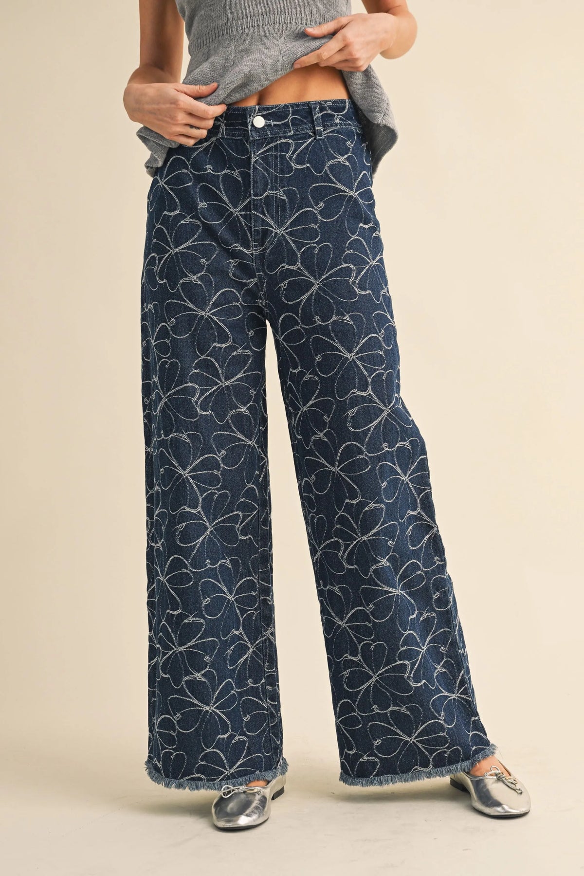 Dark blue denim wide-leg pants with white floral design and distressed hem featuring frayed edges