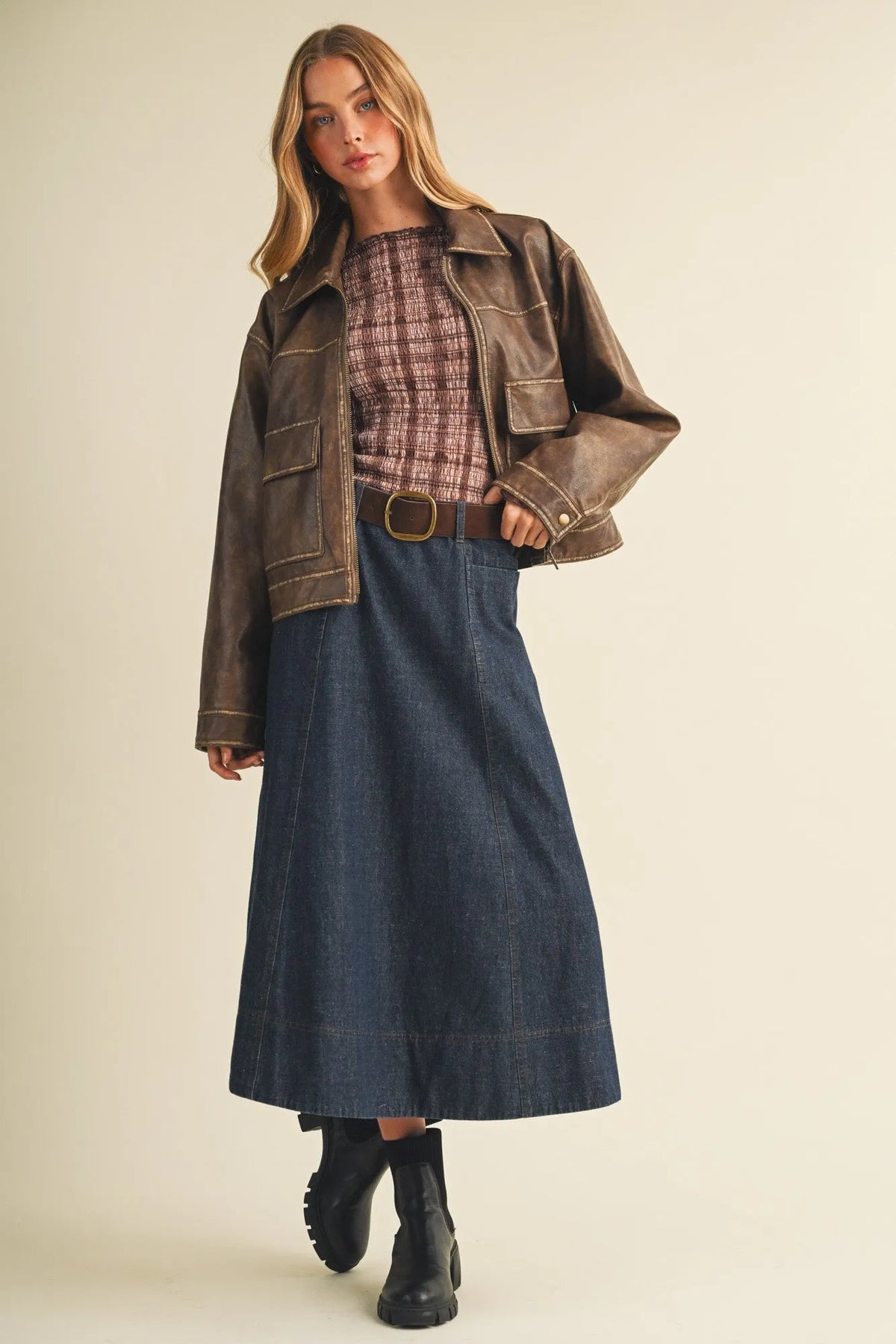 A dark brown leather jacket with classic collar and flap pockets paired with a belted indigo maxi skirt