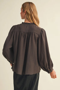 A dark gray long-sleeved blouse featuring a pintuck bib ruffle collar and gathered fabric at the shoulders