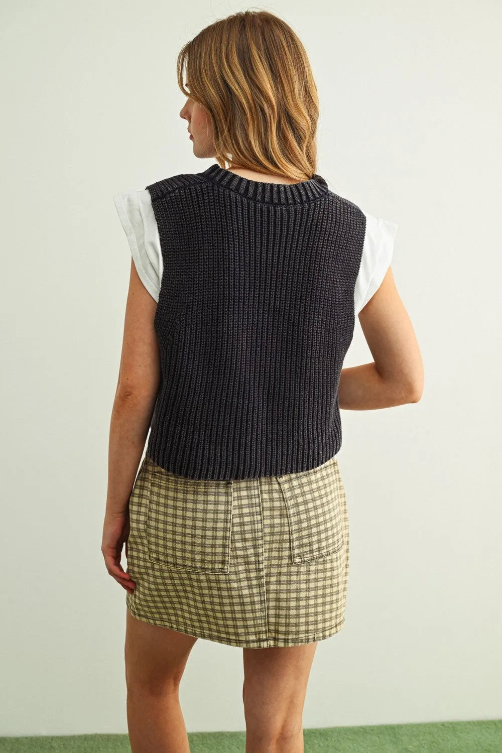 Dark gray ribbed knit v-neck sweater vest worn over a white short-sleeved jersey top combo for layered style