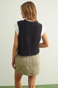 Dark gray ribbed knit v-neck sweater vest worn over a white short-sleeved jersey top combo for layered style