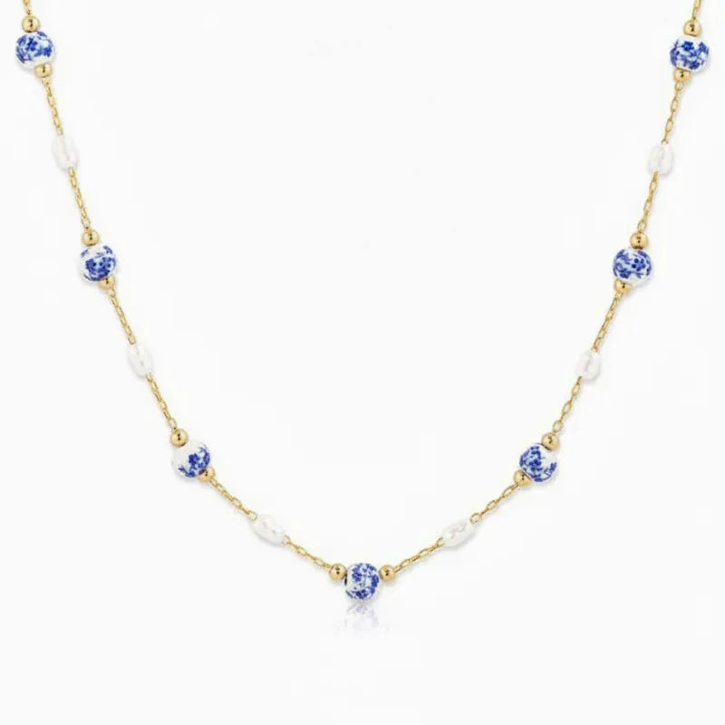 A delicate gold ceramic pearl necklace with alternating blue and white floral ceramic pearls
