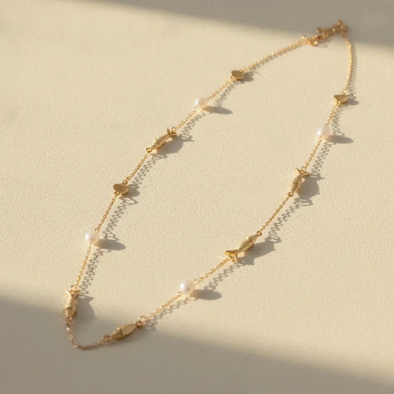 A delicate gold ocean charm station long necklace featuring small fish charms and pearl-like beads