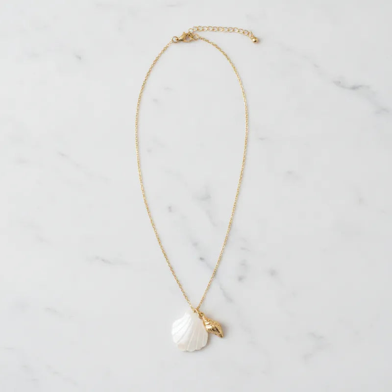 A delicate gold seashell pendant necklace featuring a white mother of pearl shell and a small golden leaf charm