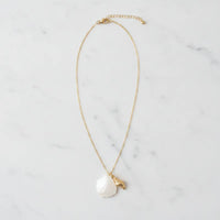 A delicate gold seashell pendant necklace featuring a white mother of pearl shell and a small golden leaf charm