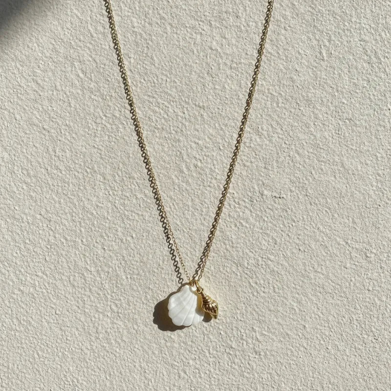 A delicate gold seashell pendant necklace with a white mother of pearl shell and a small gold conch charm