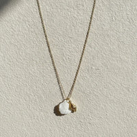 A delicate gold seashell pendant necklace with a white mother of pearl shell and a small gold conch charm