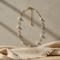 A delicate white pearl gold cube necklace with evenly spaced pearls and gold beads on beige fabric
