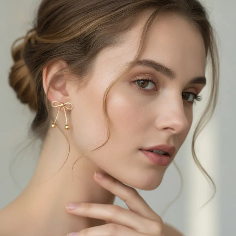 Dainty gold bow statement earrings featuring delicate gold-toned drop bow with dangling sphere tassels