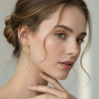 Dainty gold bow statement earrings featuring delicate gold-toned drop bow with dangling sphere tassels