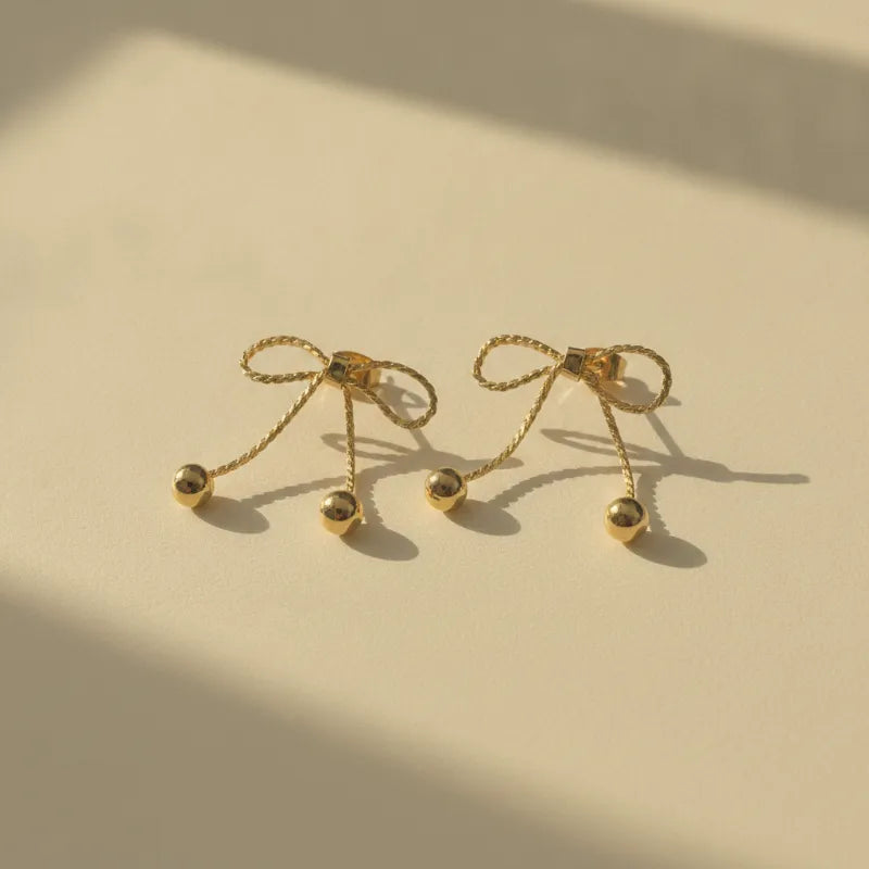 Dainty gold bow statement earrings featuring twisted rope detailing and delicate sphere tassels in gold tone