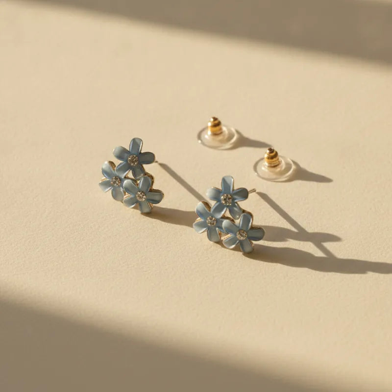 Dainty blue floral blossom stud earrings with delicate light blue enamel petals and tiny clear gemstone centers