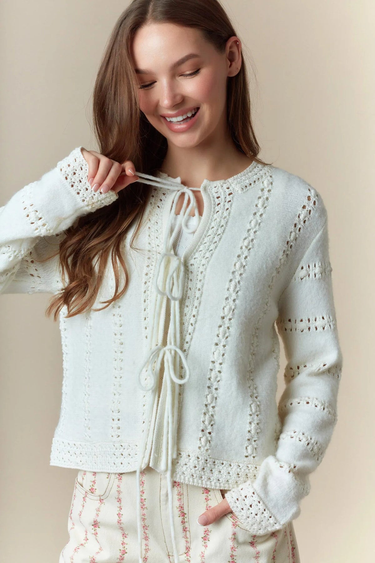 A delicate off-white knit hole stripe bows cardigan featuring intricate lace patterns and a front tie detail