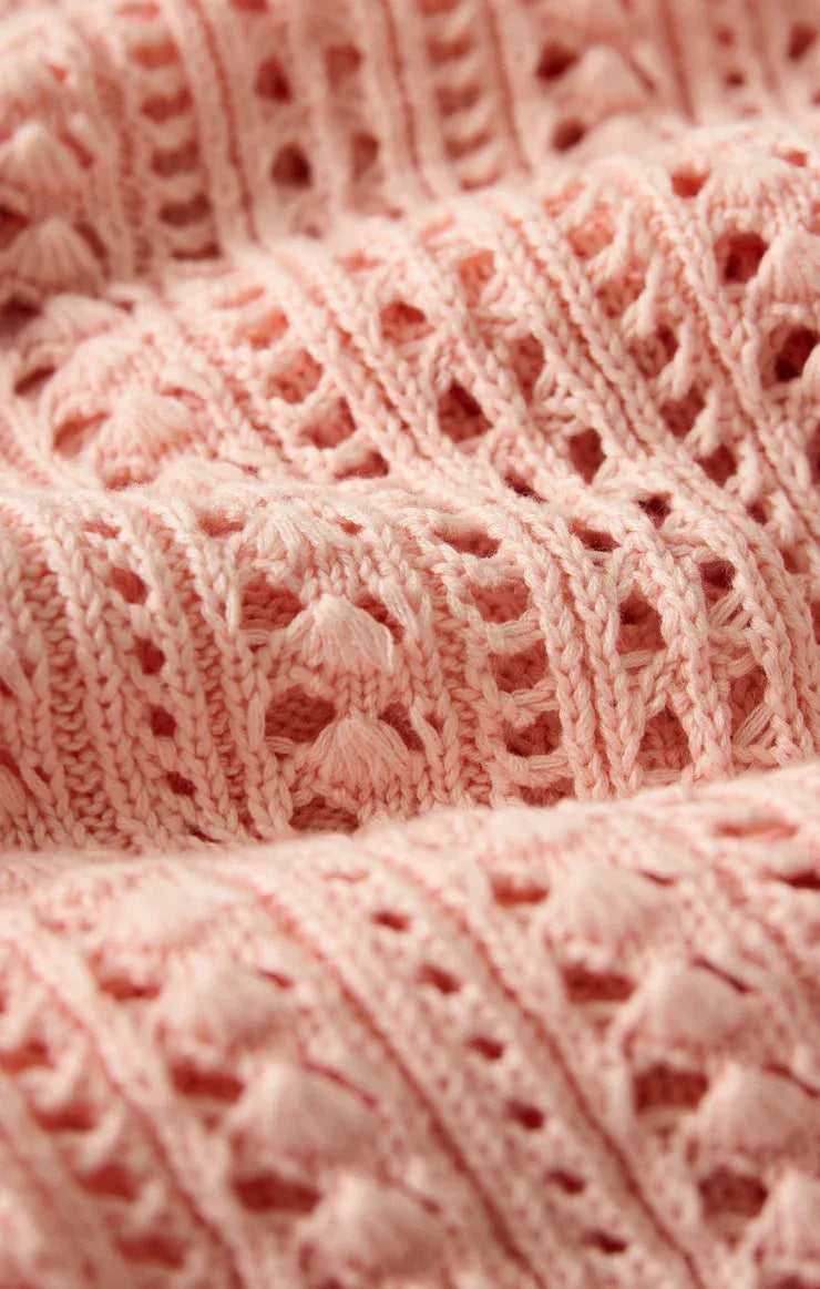 A delicate pink upland crochet sweater with intricate lace-like pattern tassels and openwork design