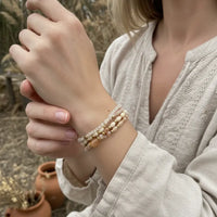 A delicate stack of boho gemstone and wood beaded bracelets with peach cream and gold tones for womens boho clothes