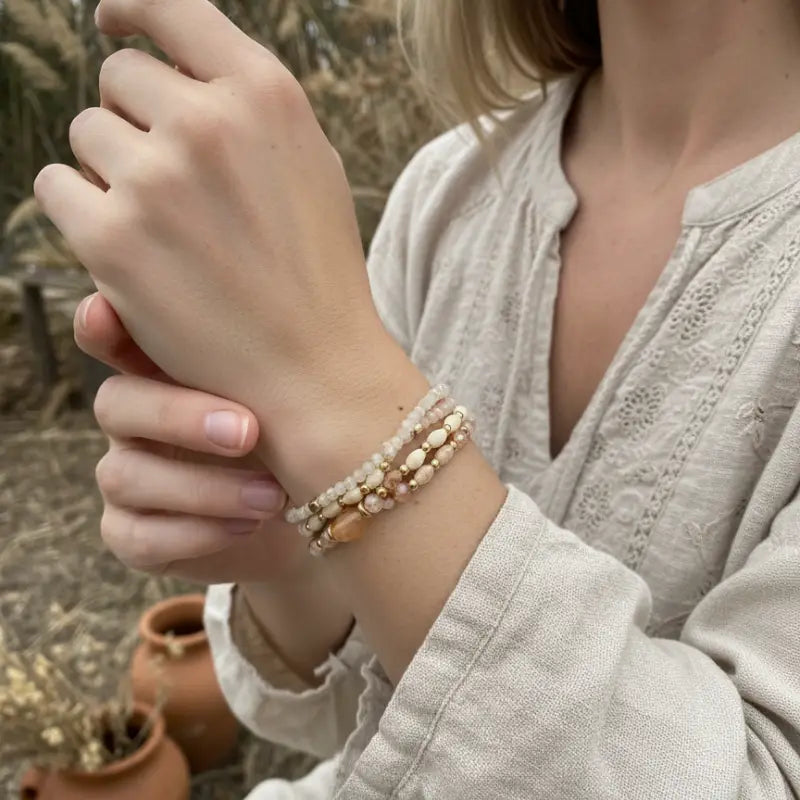 A delicate stack of boho gemstone and wood beaded bracelets with peach cream and gold tones for womens boho clothes