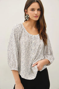A white ditsy button up peasant top with a subtle black ditsy print, puffed sleeves, and relaxed fit design