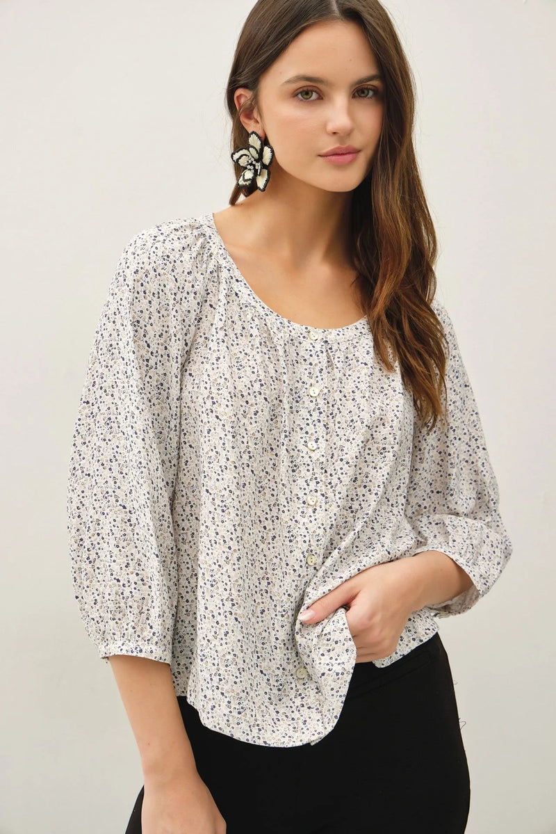 A white ditsy button up peasant top with a subtle black ditsy print, puffed sleeves, and relaxed fit design