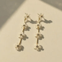 Elegant four-tier cascading white floral gold drop earrings with delicate white flower petals and clear gemstone centers