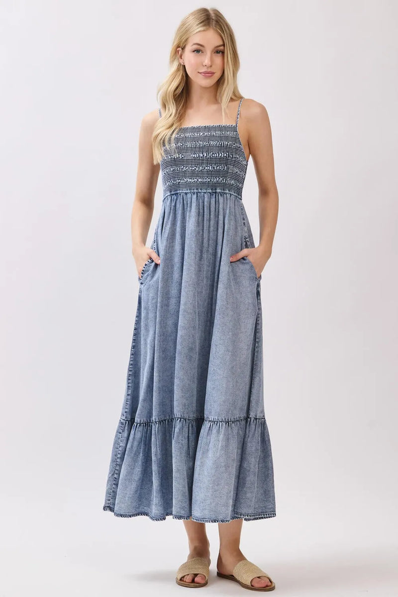 A denim tiered midi dress featuring a tencel smocked patterned bodice and a flowing tiered skirt