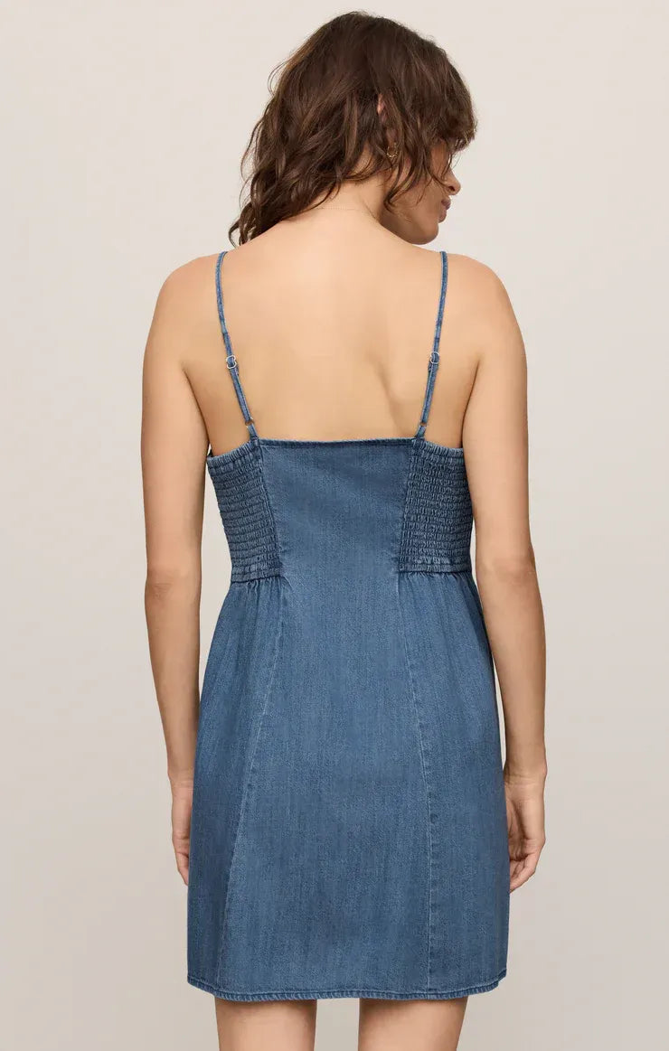 Back view of angel eyes denim mini dress featuring thin straps and smocked detailing in blue denim fabric