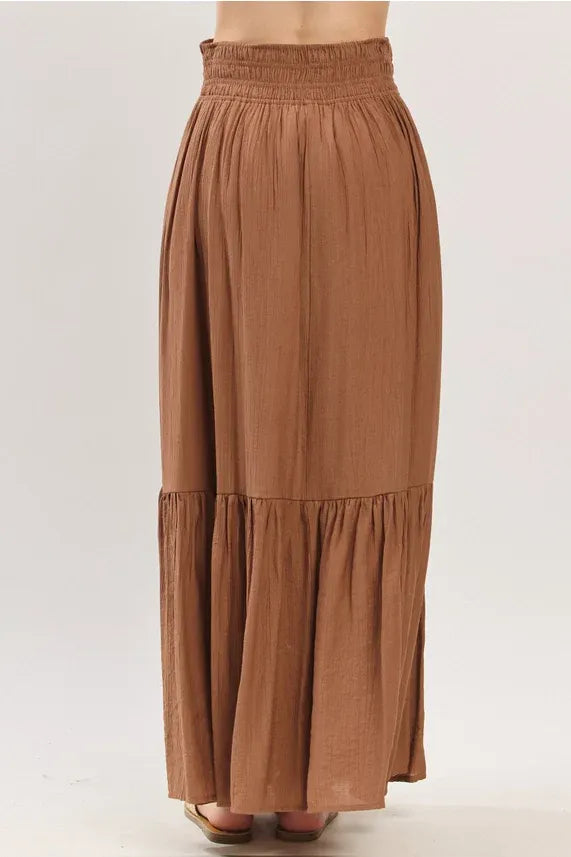 A flowing earthy brown tiered center slit maxi skirt with gathered waistband and tiered hemline