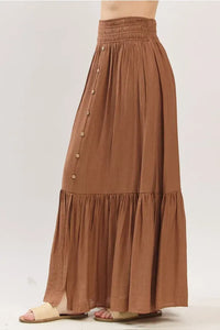 A flowing earthy brown tiered center slit maxi skirt with a gathered waistband and wooden buttons down the side