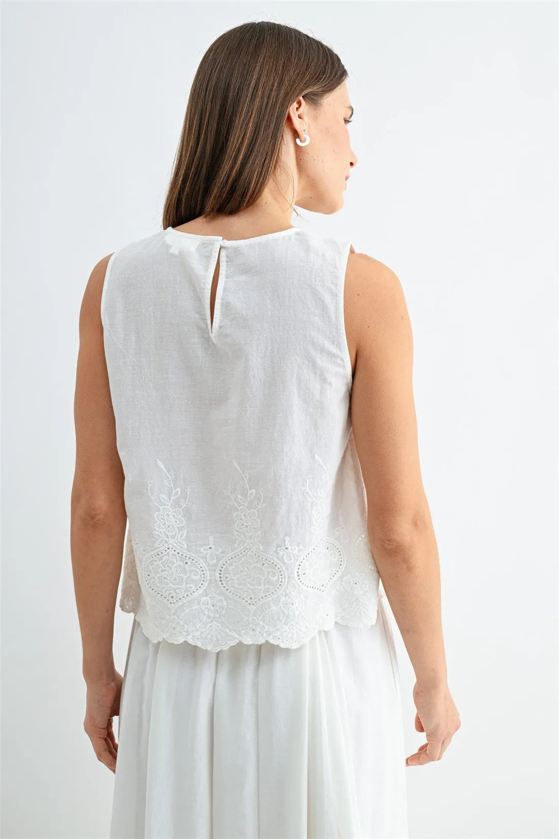 White sleeveless button blouse featuring delicate eyelet hem lace embroidery and a small back slit detail